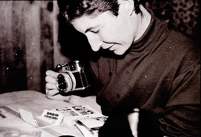 Vintage black-and-white portrait of an individual examining a stack of photographs using a vintage 35mm camera. The scene sug...