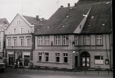 Three-story corner building in classic German urban architecture, featuring gabled roofs, symmetrical windows, and a sign rea...