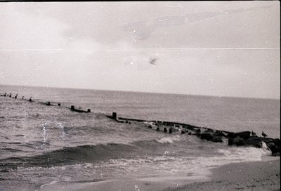 Black-and-white coastal scene featuring a weathered wooden pier extending into choppy waters. The structure appears aged, wit...