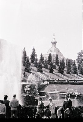 Vintage black-and-white shot of a grand fountain in a landscaped park, with a prominent Orthodox church featuring onion domes...