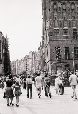 Vintage street scene featuring Gothic Revival architecture with ornate stonework and a prominent fountain statue. Crowd of ca...