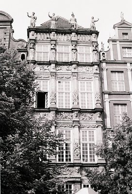Baroque-style building facade with intricate stone carvings, statues, and symmetrical windows. Ornate reliefs depict classica...