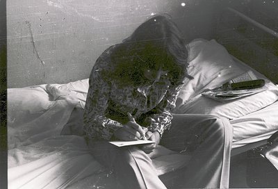 Vintage black-and-white photo of a person sleeping on a bed with a floral-patterned blanket. Reflections on the window reveal...
