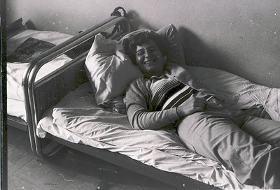 Vintage black-and-white hospital bed with metal railings, showing a relaxed individual in striped pajamas resting on pillows....