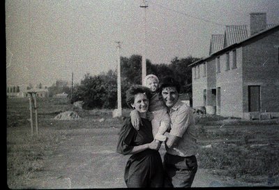 A black-and-white snapshot of three individuals posing outdoors in a rural setting, likely mid-20th century. The woman and ma...