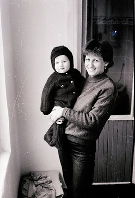 Black-and-white portrait of a woman cradling a toddler indoors, likely mid-20th century. The woman wears a knitted sweater wi...