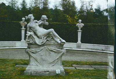 Neoclassical stone fountain sculpture depicting reclining female figure with draped drapery, flanked by two busts on pedestal...
