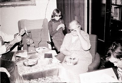 Vintage black-and-white indoor scene featuring a seated elderly woman in glasses holding her face, surrounded by three childr...