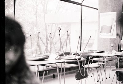 Mid-century classroom with tiered desks and chairs, likely –. Overhead projector and chalkboard setup suggests educational fo...