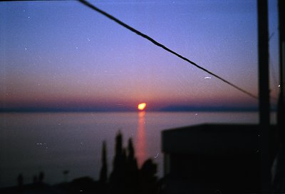 Vintage-style shot of a sunrise/sunset beam through a window frame, silhouetted by silhouetted trees and a faint coastal hori...