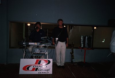 Live band performance featuring a keyboardist (Korg M3) and saxophonist on stage, likely 1990s. Sign reads "Diana Group Semil...