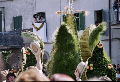 Vibrant folk festival with towering, intricately woven straw effigies adorned with greenery, fruits, and wheat bundles. Crowd...