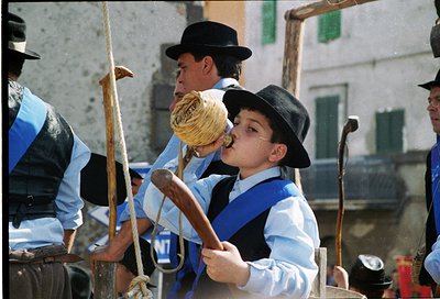 Traditional folk musicians in coordinated blue-and-white attire play wooden flutes, likely during a cultural festival. The bl...