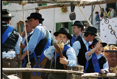 Traditional wooden boat crew in coordinated blue-and-white attire, including wide-brimmed hats, operating a hand-cranked mech...