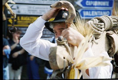 A man in traditional attire, likely a shepherd, handles a sheep in a public or market setting. His white tunic, dark hat, and...