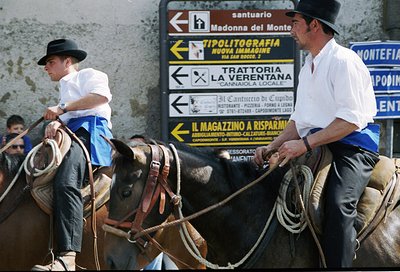 Two men in traditional Italian riding gear guide horses near a roadside signpost in . Signs indicate directions to local attr...