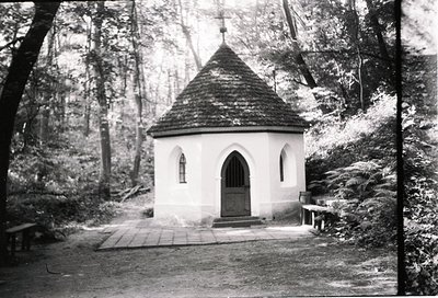 Isolated 19th-century alpine chapel with Gothic Revival arched doorway, conical slate roof, and cross-topped spire, nestled i...