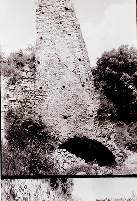 Ruined stone tower with visible arched doorway, likely medieval fortress remains. Weathered bricks and overgrown foliage sugg...