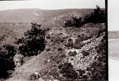 Vintage black-and-white landscape showing rugged terrain with sparse vegetation and rocky outcrops. The scene captures a stee...