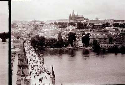 Vintage black-and-white aerial view of Prague’s Charles Bridge and Vltava River, crowded with pedestrians. Gothic spires of P...