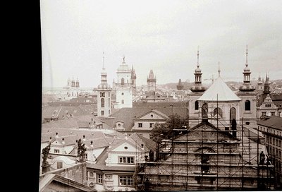 Early 20th-century European cityscape featuring Baroque-style domes and spires. Prominent church with scaffolding suggests re...