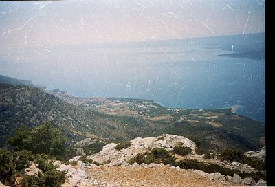 Vintage panoramic shot of rugged coastal terrain with layered hills, rocky outcrops, and distant sea. Evidence of age: scratc...