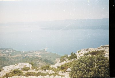 Vintage coastal landscape shot from elevated rocky terrain, showcasing a serene sea meeting distant land. Vegetation includes...