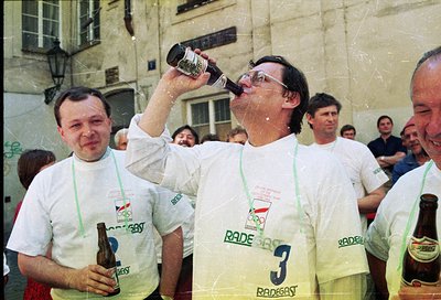 Celebratory moment at the 1980 Moscow Olympics, featuring two men in matching white "Rade Gast" event shirts drinking beer. T...