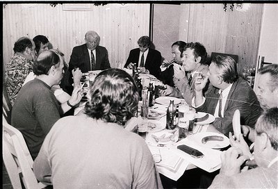 Group of 15+ men and women seated at a long table in a formal indoor setting, likely a 1970s–1980s business or diplomatic gat...
