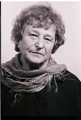 Portrait of an elderly woman in mid-20th century attire—gray scarf, dark blazer, and short hair. Grainy black-and-white sugge...