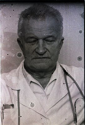 Vintage black-and-white portrait of an older man in a lab coat, stethoscope draped around neck. Expression is solemn, gaze do...