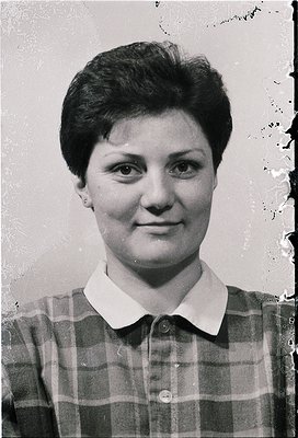 Portrait of a woman in a mid-century plaid blouse, likely from the 1960s–1970s. Short, neatly styled hair and minimalist earr...