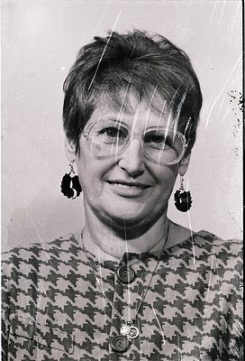 Portrait of a woman in mid-20th century fashion, wearing round-framed glasses and large, geometric-pattern earrings. Her patt...