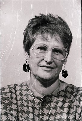 Portrait of a woman in a patterned blouse, short hairstyle, and round glasses, wearing distinctive black earrings with circul...