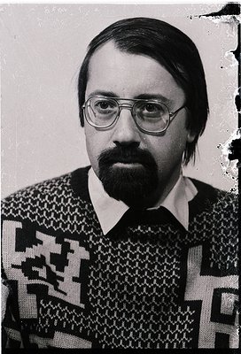 Portrait of a man in a patterned sweater and round glasses, likely from the 1970s–1980s. Geometric, textured knit suggests mi...
