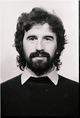 Portrait of a man with a full beard and mustache, wearing a striped collared shirt and dark sweater. Style suggests mid-20th ...
