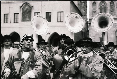 Vintage black-and-white street band in traditional European attire, playing brass instruments and cymbals. Uniforms feature p...
