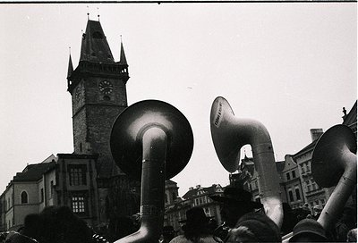 Black-and-white street scene featuring large megaphones in foreground, likely from a public gathering or rally. Prominent clo...
