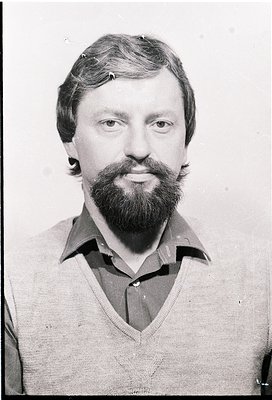 Portrait of a man with a full beard and mustache, wearing a collared sweater. Mid-20th century styling suggests or . Plain ba...