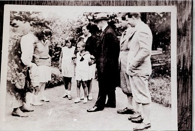 Mid-20th century black-and-white photo of a family group outdoors, likely mid-1950s. Six individuals—adults in long-sleeve sh...