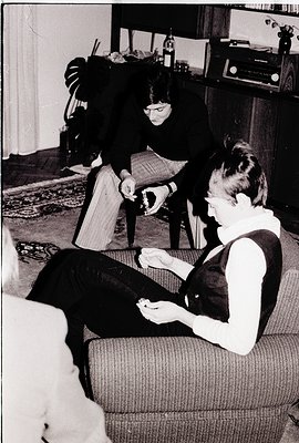 Vintage black-and-white photo of two women in a mid-century living room: one seated on a tufted sofa holding a small object, ...