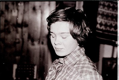 Portrait of a young woman in a plaid shirt, captured in black-and-white. Her short, textured hair and contemplative expressio...