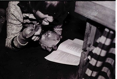 A child meticulously crafts with clay near an open book, likely a craft or art project. The scene suggests a mid-20th century...