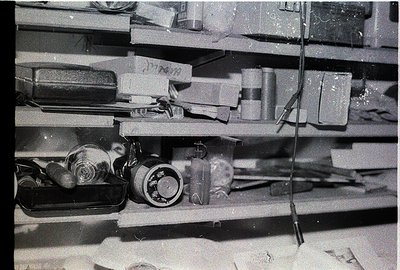 Vintage industrial shelf stocked with cylindrical metal containers, valves, and mechanical parts. Possible mid-20th century f...
