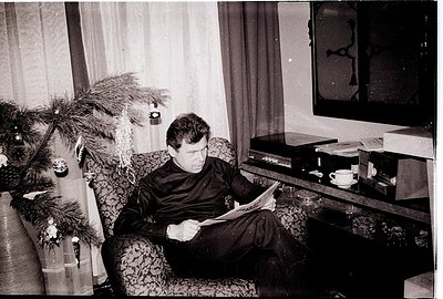 Mid-century living room scene: man in formalwear reads newspaper beside a decorated Christmas tree. Vintage TV console holds ...