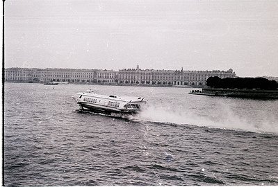 A vintage black-and-white photo of a high-speed passenger boat cutting through calm waters, with the iconic neoclassical faça...
