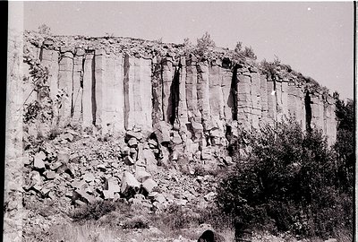 Vertical rock strata with distinct sedimentary layers and erosion patterns, likely limestone or sandstone. Vegetation at base...