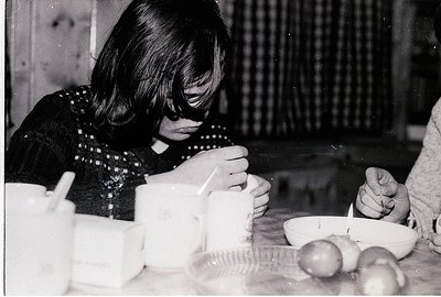 Vintage black-and-white photo of two individuals seated at a rustic wooden table, engaged in a meal. The person on the left w...