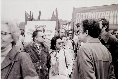 Black-and-white protest scene featuring a crowd holding signs with Cyrillic text, likely Eastern Bloc era. Central figures we...