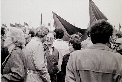 Black-and-white photo of a mid-20th-century public gathering, likely 1960s–1970s. Crowd of adults in casual attire (jackets, ...